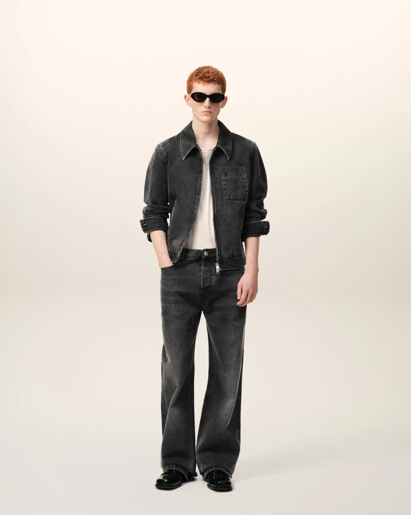 Red-haired model wearing a black denim jacket, white shirt, and dark jeans with sunglasses, facing the camera.