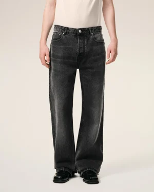 Lower torso and legs of a person wearing dark wash jeans and black shoes against a beige background, front view.