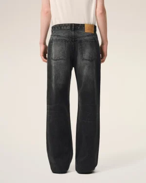 Back view of a person wearing dark wash jeans with two back pockets and a tan leather brand patch at the waistband on the right side.