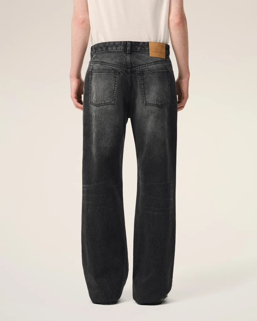 Back view of a person wearing dark wash jeans with two back pockets and a tan leather brand patch at the waistband on the right side.