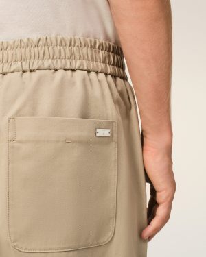 Close-up of beige khaki pants with an elastic waistband and back patch pocket, a portion of the arm visible nearby.