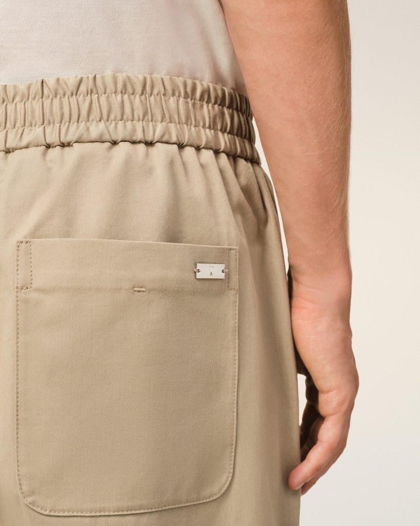Close-up of beige khaki pants with an elastic waistband and back patch pocket, a portion of the arm visible nearby.