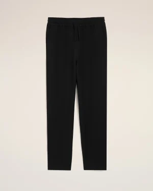 Full-length image of black jogger-style pants with an elastic drawstring waist against a light beige background, displayed front-on for product viewing.