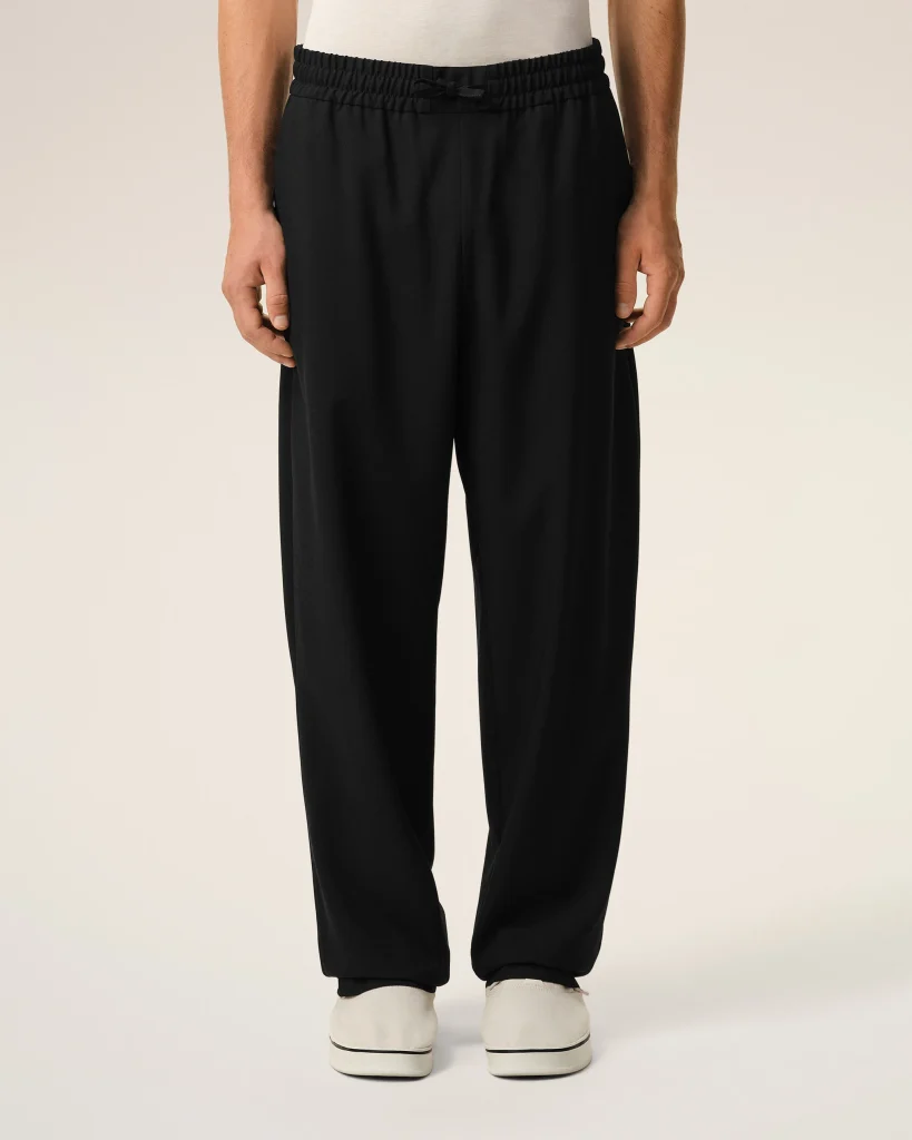 Back view of person wearing black drawstring joggers and white sneakers against a light backdrop.