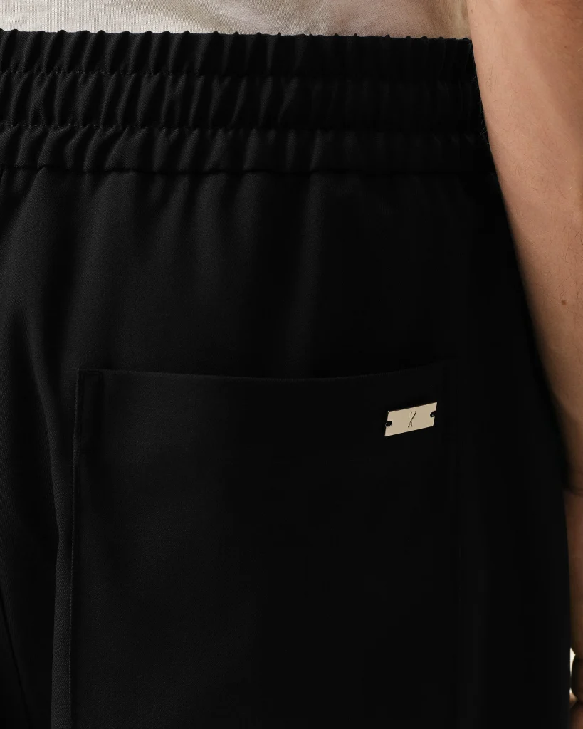 Close-up of black elastic-waist pants with a rear pocket and a small metal label, worn by a person whose arm is visible on the right side