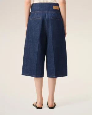 Back view of a person wearing dark blue high-waisted wide-leg denim culottes with orange stitching and a small brown leather brand patch on the waistband.