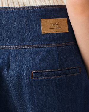 Back pocket area of dark blue denim jeans with a tan leather brand patch reading 'ami' and 'alexandre mattiussi'.