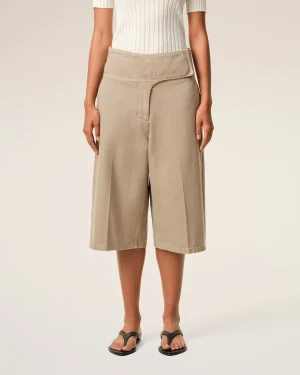 Person wearing beige wide-leg shorts with a white ribbed top and black sandals, shown from waist to feet against a neutral background.