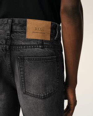 Back view of a person wearing dark denim jeans with a tan leather patch that reads 'ami alexandre mattiussi' on the waistband.