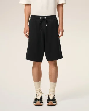 Lower half of a person wearing black drawstring shorts, a white T-shirt, cream socks, and black sneakers, standing against a light background.