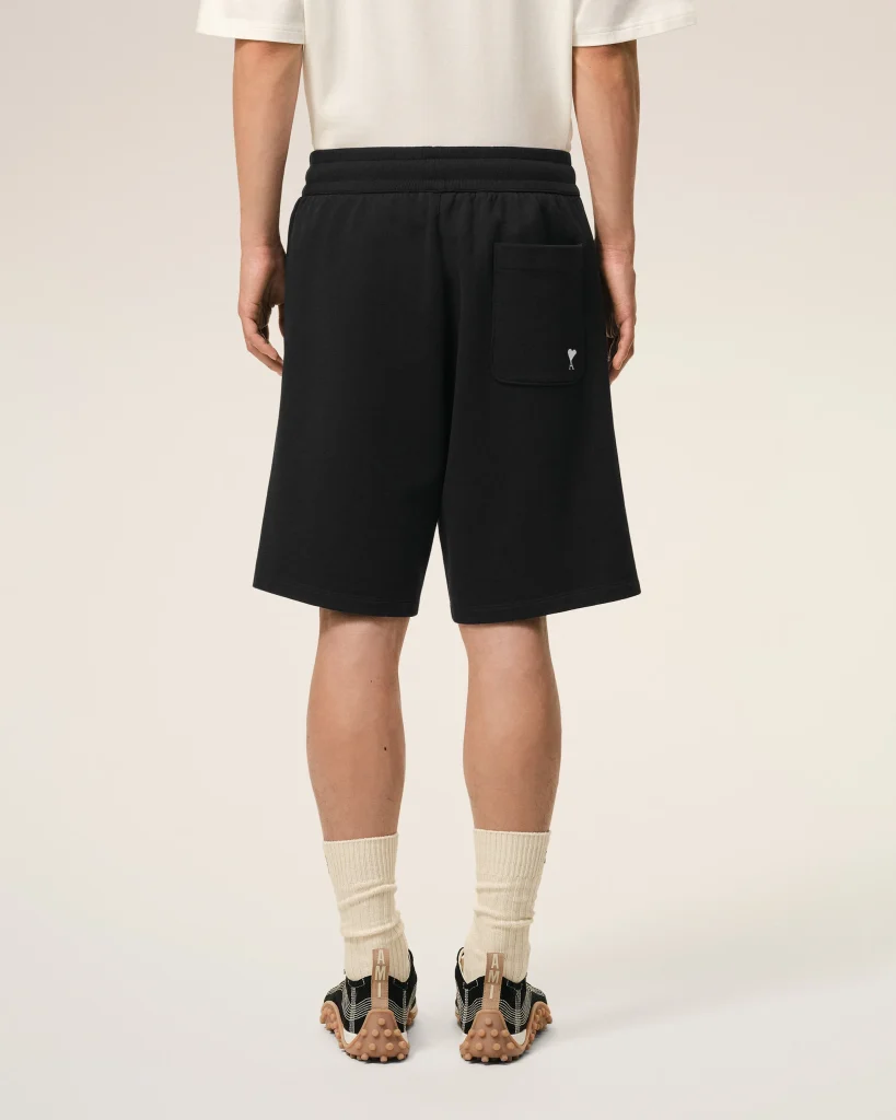 Back view of a person wearing black shorts with a rear pocket, white shirt, beige socks, and black sandals with tan soles.