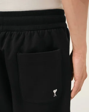 Close-up of a black fabric pocket (likely jogger) with a small white heart-shaped emblem near the hem, alongside part of a beige sleeve and arm visible.