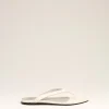 White flip-flop sandals with a minimalist thong strap placed on a pale beige backdrop, product photo for footwear.