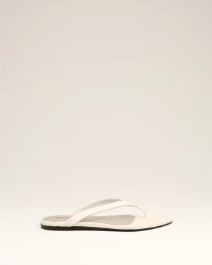 White flip-flop sandals with a minimalist thong strap placed on a pale beige backdrop, product photo for footwear.