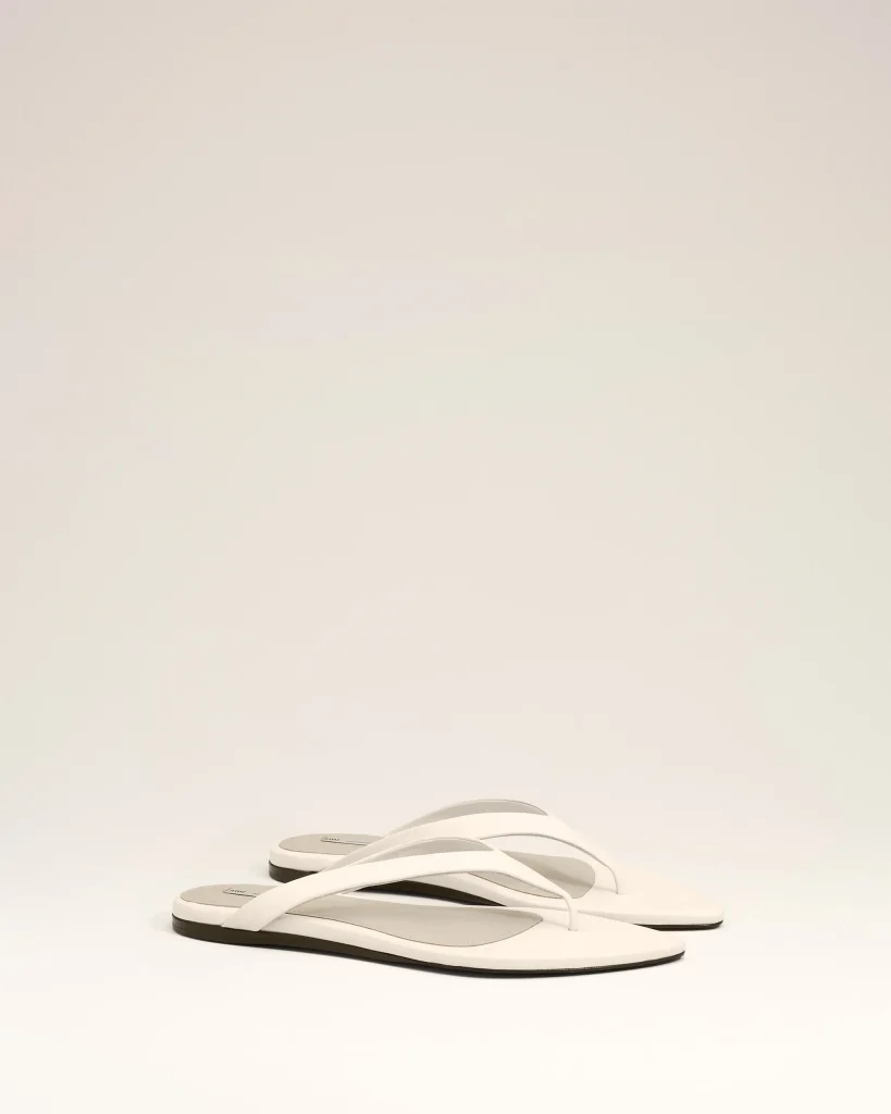 White flip-flops with gray soles arranged diagonally on a pale background.