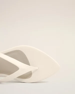 White sandal close-up showing leather straps and stitching on a pale background.