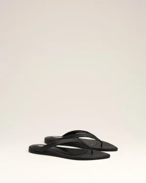 Pair of black flip-flop sandals with thin straps lying on a white surface.