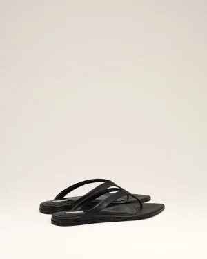 Black flat-sole sandals with multiple straps arranged on a light beige background, photographed from above of a studio setup.