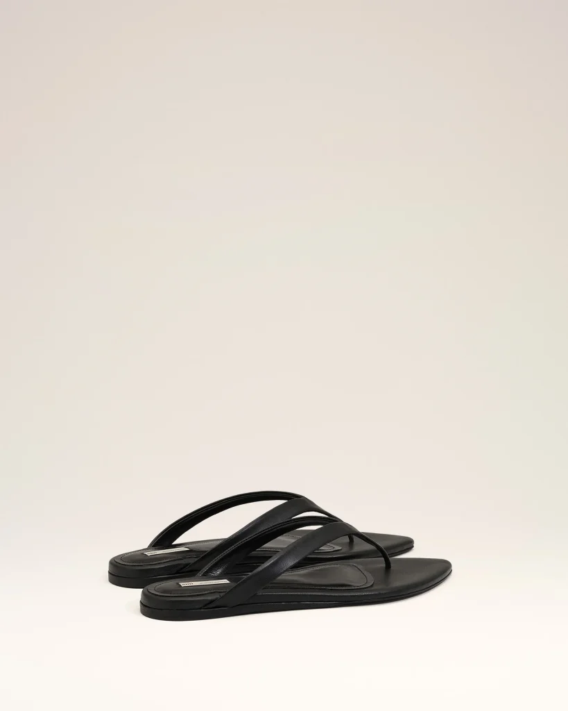 Black flat-sole sandals with multiple straps arranged on a light beige background, photographed from above of a studio setup.