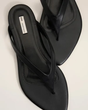 Black leather sandals with multiple crisscross straps and a small white fabric label on the insole reading 'ami' (brand tag).