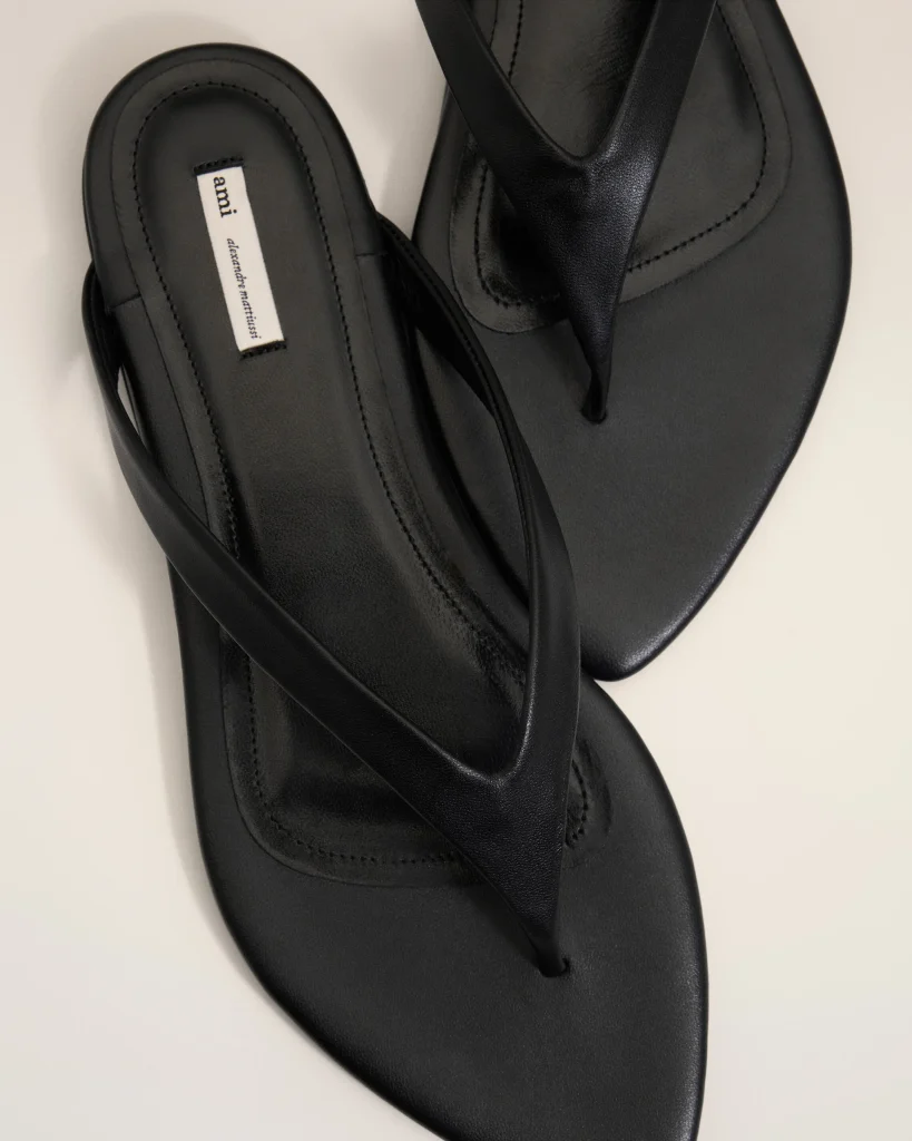 Black leather sandals with multiple crisscross straps and a small white fabric label on the insole reading 'ami' (brand tag).