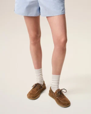 Person standing, wearing light blue striped shorts, white socks, and brown boat shoes against a neutral background.