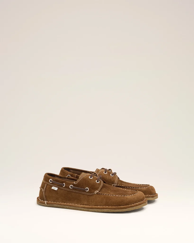 Pair of brown suede moccasin-style boat shoes with white stitching on a light background.