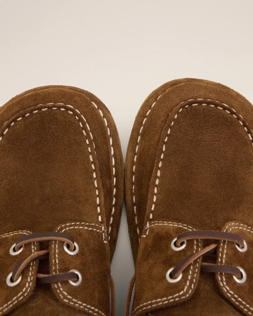 Close-up of brown suede moccasin shoes with white contrast stitching and laces