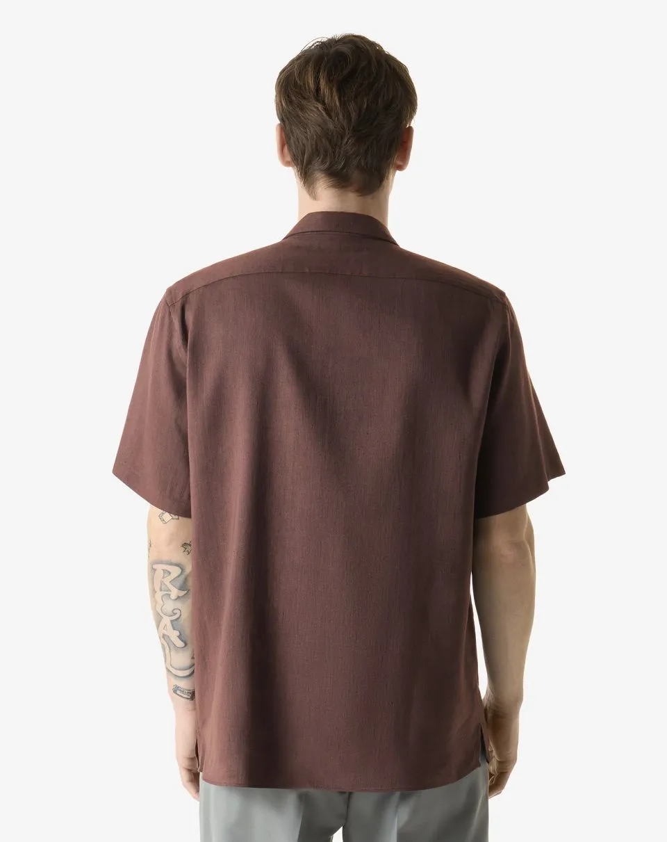 IMG_1574 - New Trend Man shown from behind wearing a brown short-sleeve shirt; tattoos visible on the left forearm.