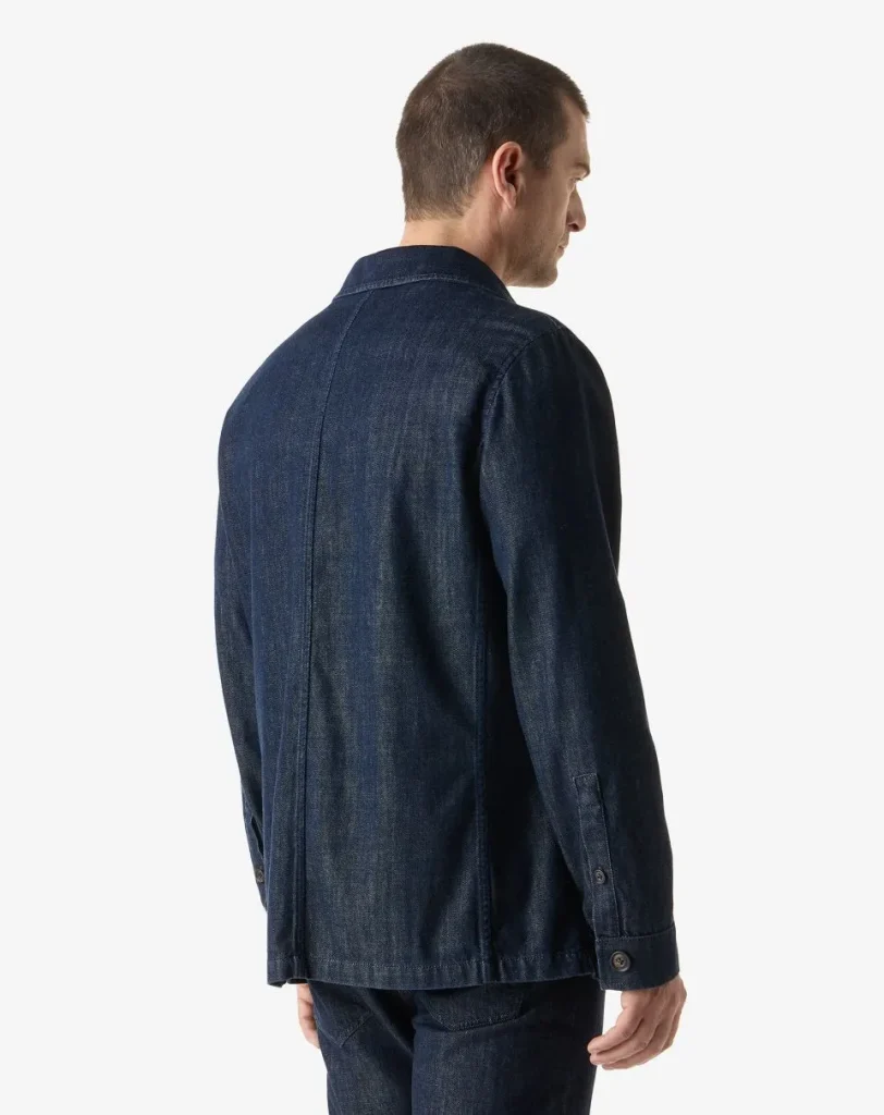 Back view of a man wearing a dark blue denim jacket and matching jeans, facing to the right.