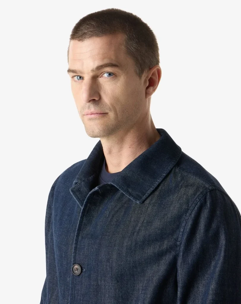 Portrait of a man with short dark hair wearing a dark denim jacket against a white background, looking slightly to the left.