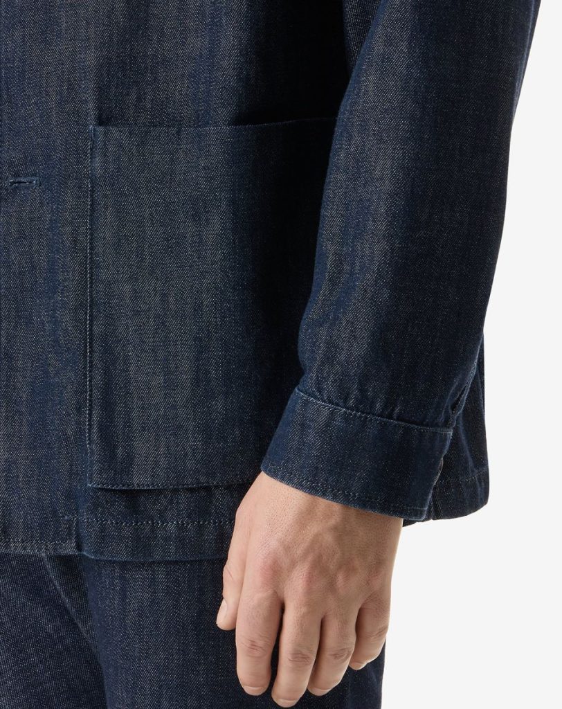 Close-up of a dark denim jacket sleeve with a front patch pocket and visible stitching.