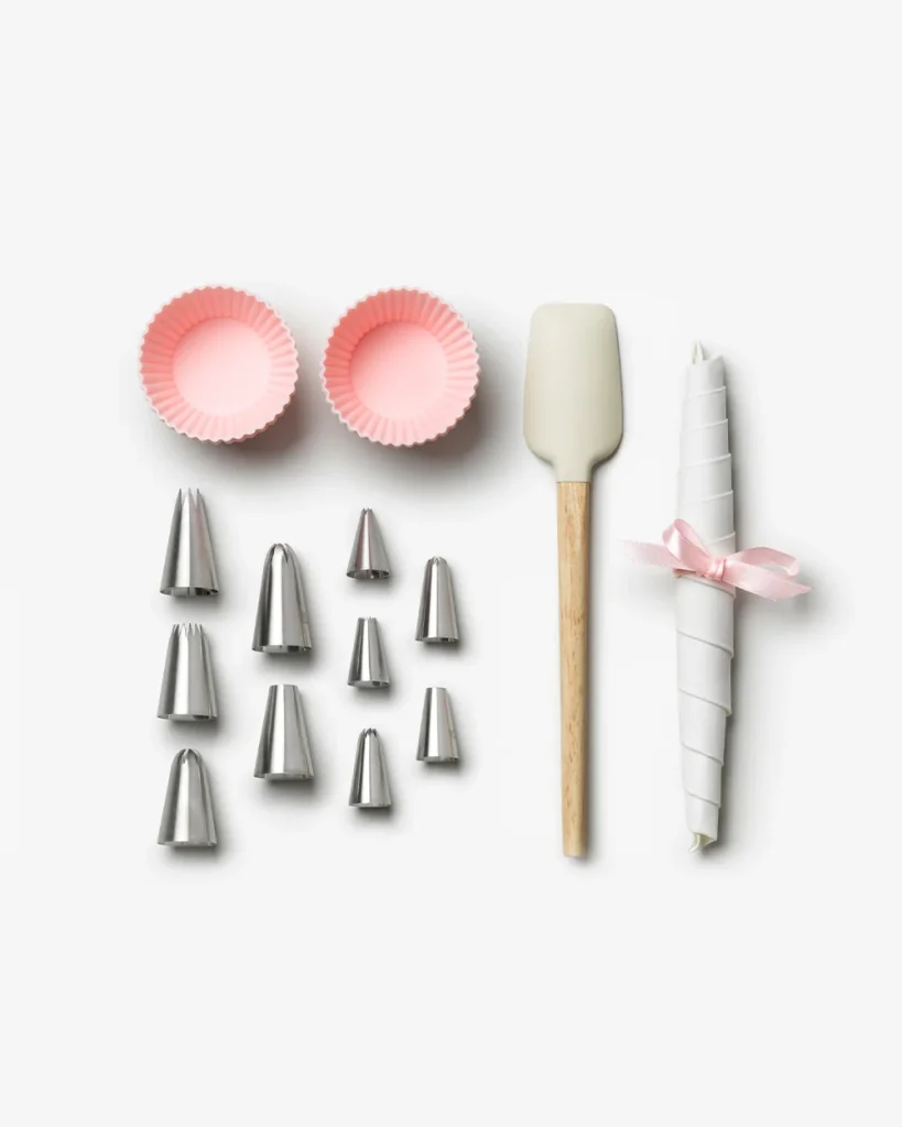Set of cake decorating tools: two pink cupcake liners, multiple metal piping tips, a silicone spatula, and a tied icing bag.