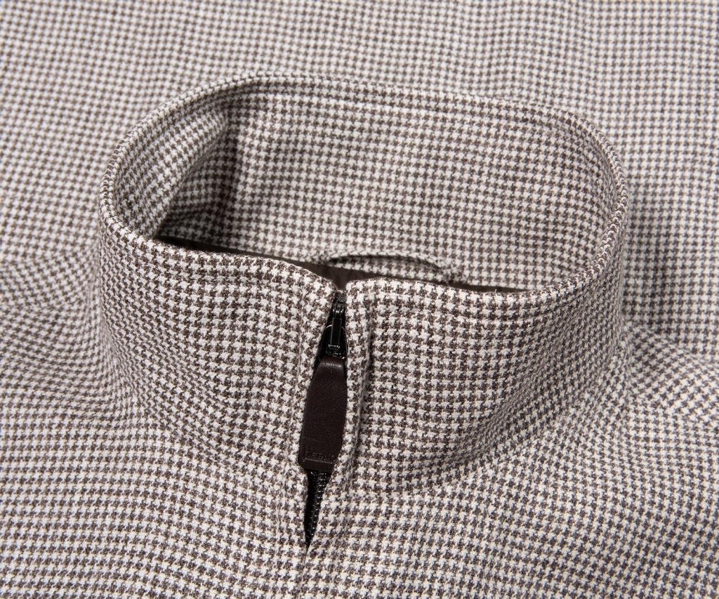 Close-up of a beige-brown houndstooth fabric with a front zipper, likely a jacket or coat detail.
