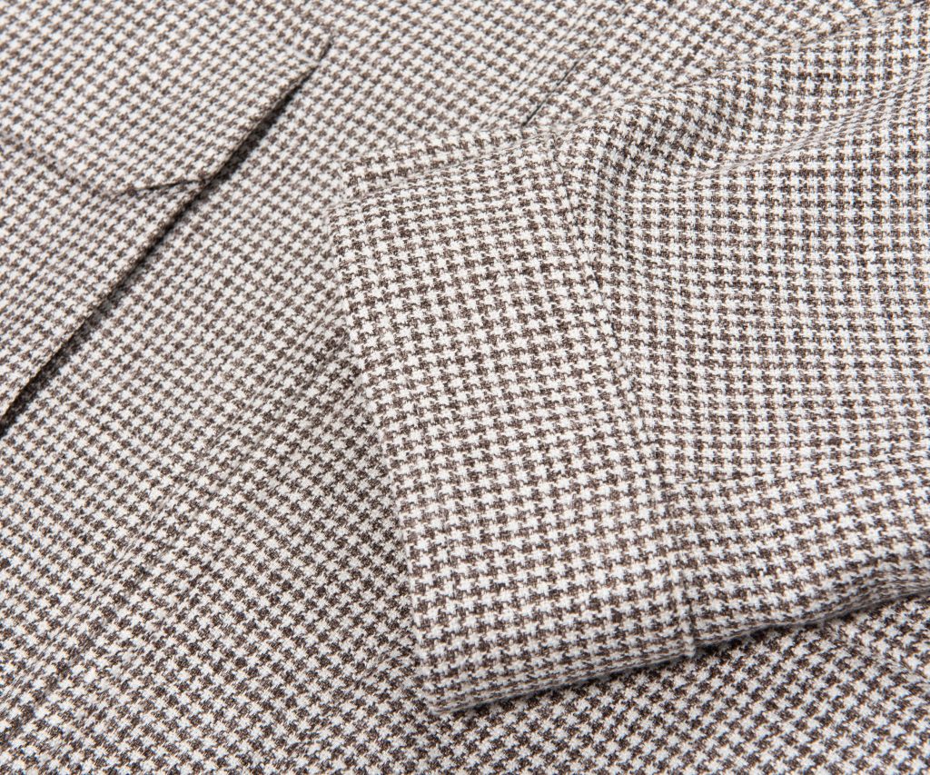 Close-up of brown and white houndstooth fabric with folded edges, showing a classic textured pattern.