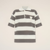 Striped knit polo shirt with cream and gray horizontal stripes and a small heart patch on the chest, against a pale beige backdrop.