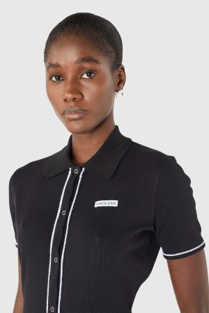Portrait of a woman with short hair wearing a black polo with white piping and a MARINE SERRE label on the chest, against a light background.
