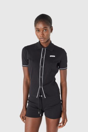 Young woman in a black polo shirt with white piping, posing against a light gray backdrop.