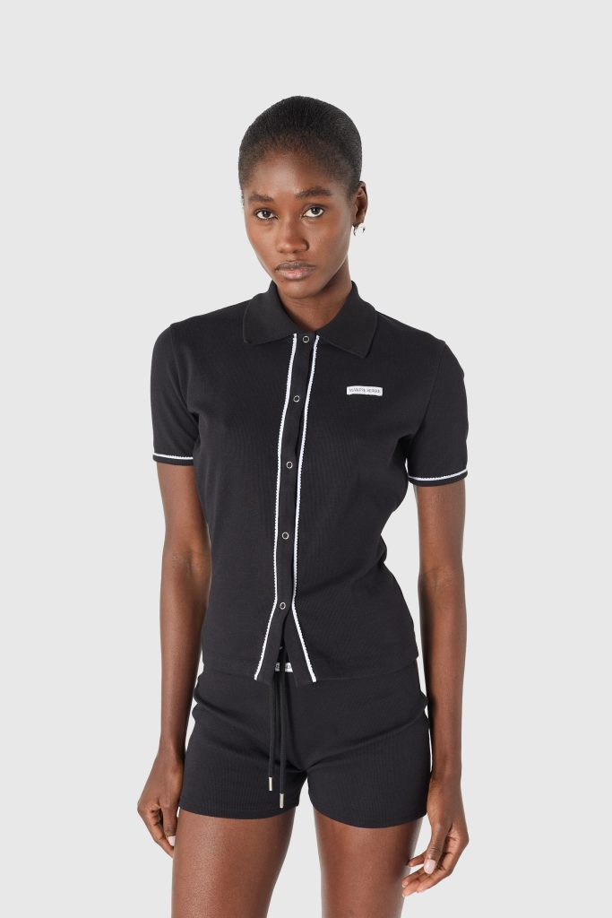 Young woman in a black polo shirt with white piping, posing against a light gray backdrop.