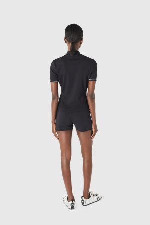 Back view of a person wearing a black polo shirt and black shorts, white sneakers, standing against a light gray background with arms at sides.