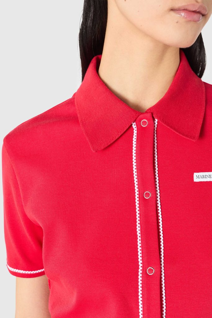 Close-up of a red polo shirt showing a collared neck, white zipper trim, and a small MARINE label.