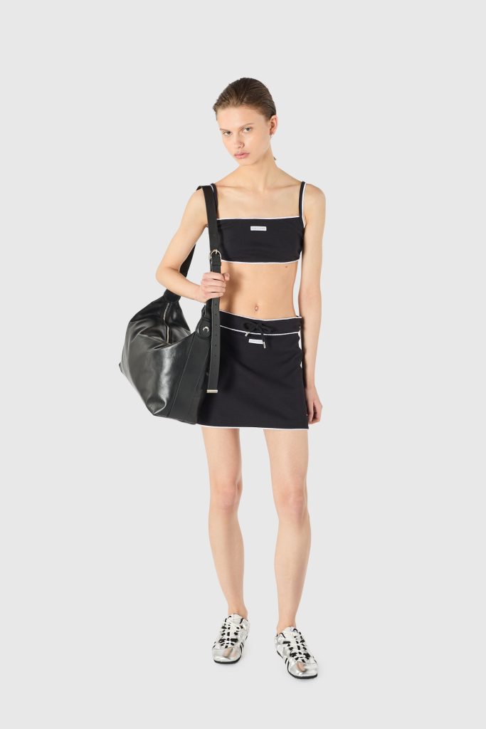 Woman in a black two-piece athletic outfit with white trim, carrying a large black shoulder bag over her chest.
