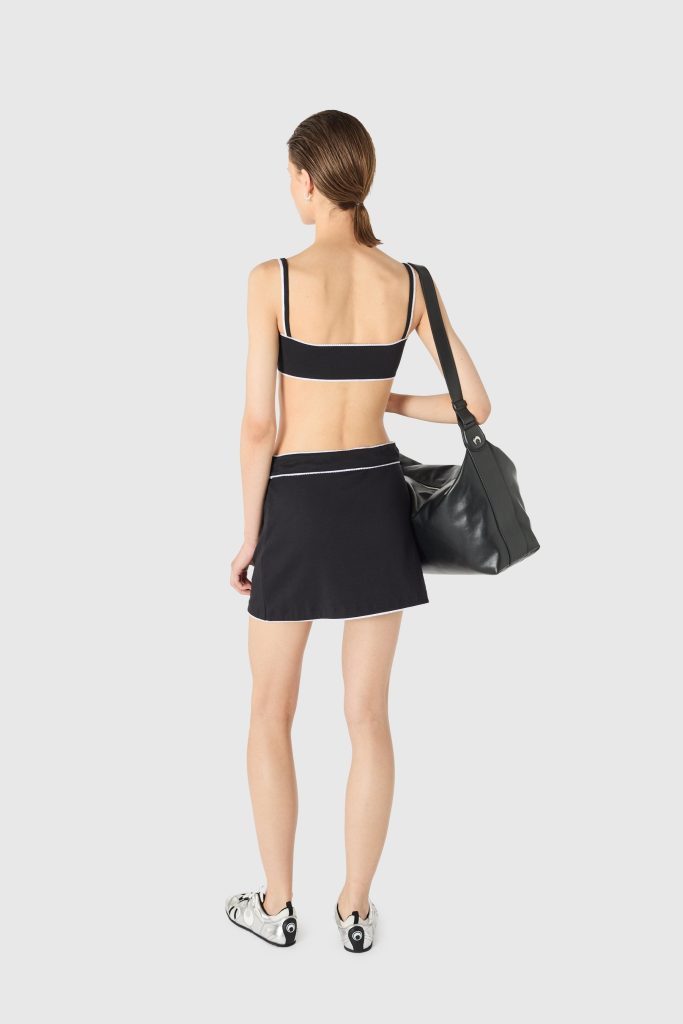 Woman seen from behind wearing a black sports bra and matching skirt with white trim, carrying a large black shoulder bag.