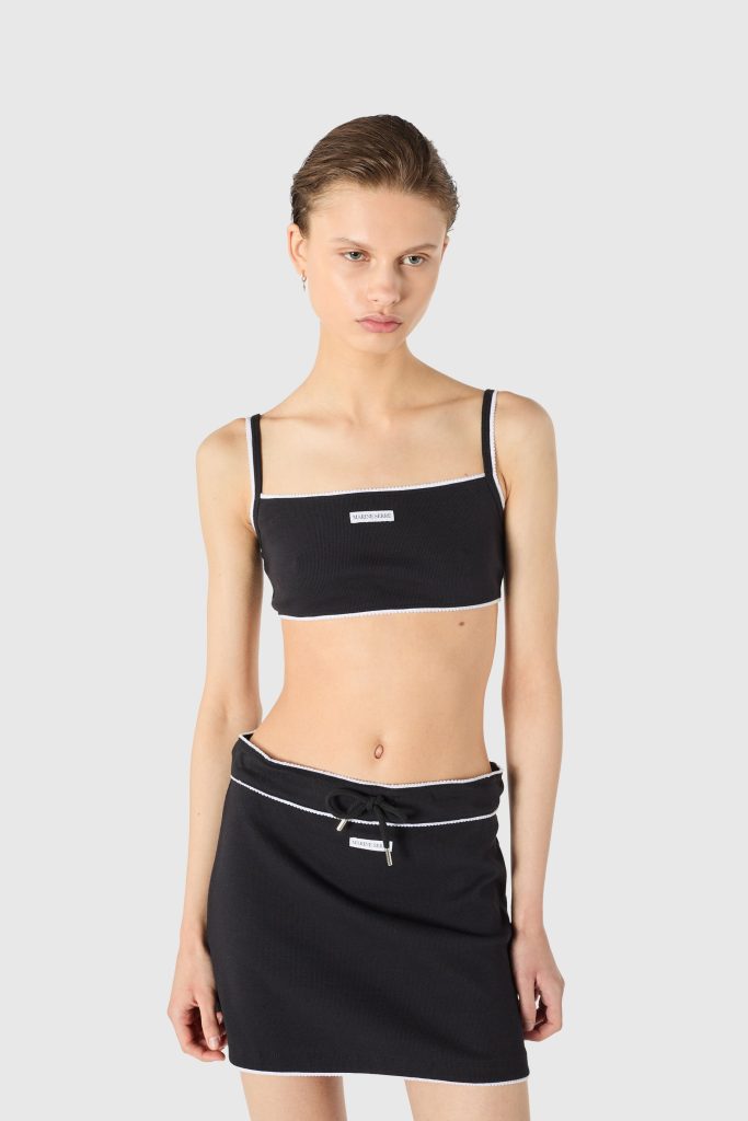 Front view of a woman in a black two-piece swimsuit with white trim, standing against a light background.