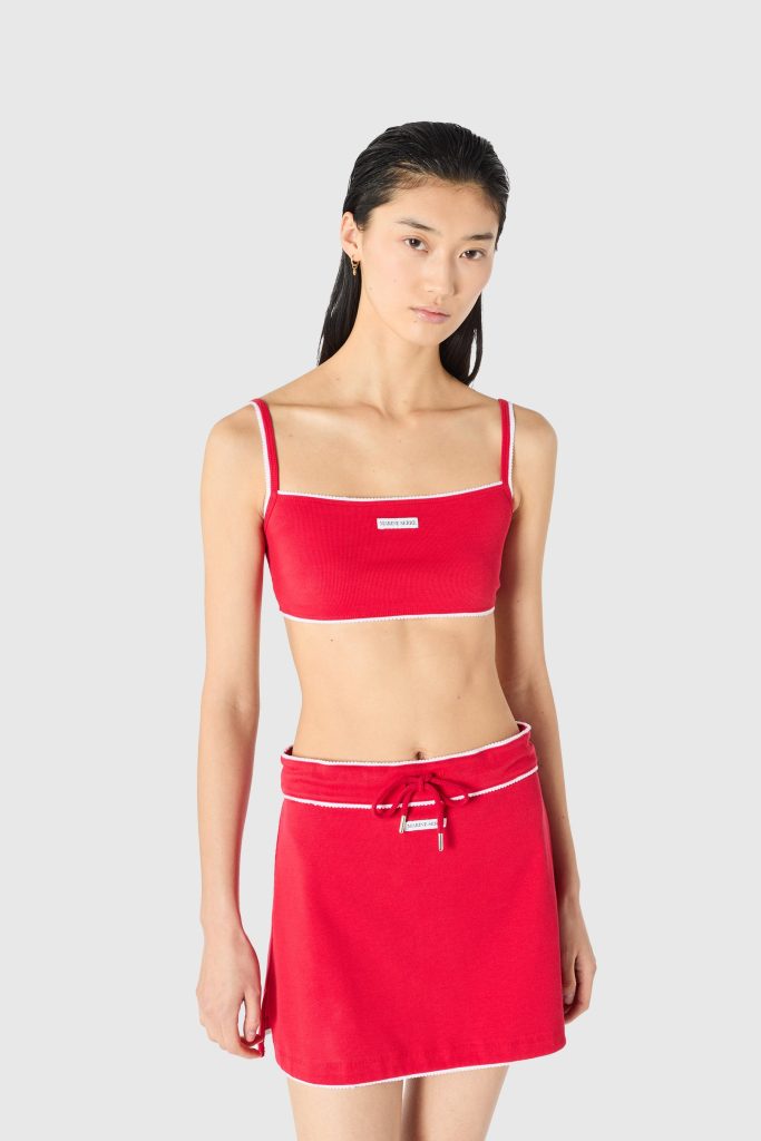 Model wearing a red two-piece swimsuit: square-neck top with white trim and matching red skirt with a drawstring, against a light gray background.