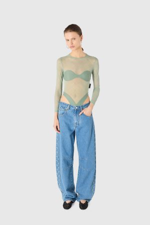 Model wearing a light green sheer long-sleeve top over a bra, paired with high-waisted blue jeans and black flats.