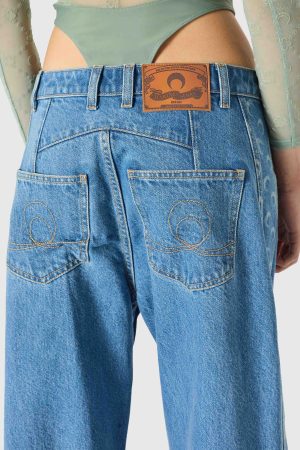 Rear view of a person wearing high-waisted blue jeans with two back pockets and a brown leather brand patch on the waistband; a green top peeks above the jeans.