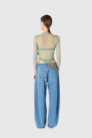Back view of a person in a sheer mint green long-sleeve top and high-waisted blue jeans, hair tied at the nape, wearing large hoop earrings.