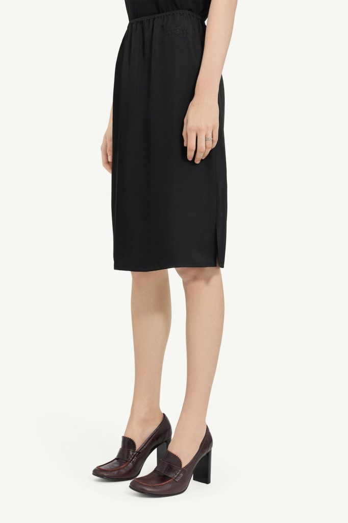 Side view of a person wearing a black knee-length skirt with a small side slit and burgundy heeled loafers.