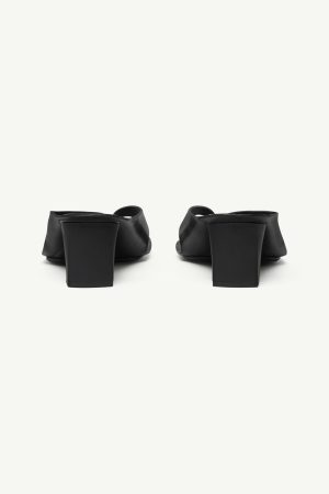 Pair of black heeled mules seen from behind, featuring chunky square heels and open backs.